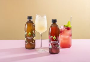 kombucha w butelkach i kieliszkach na różowo żółtym tle