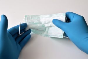 pracownik służby zdrowia z lateksowych rękawiczkach trzymający maseczkę jednorazową