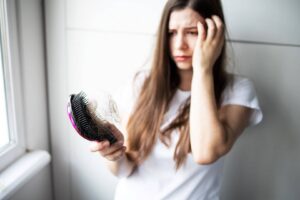 zmartwiona kobieta trzymająca szczotkę pełną włosów