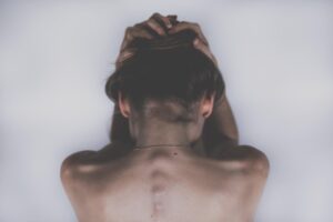 Widok od tyłu na kobietę trzymającą dłonie na głowie, symbolizującą silny ból głowy i migrenę